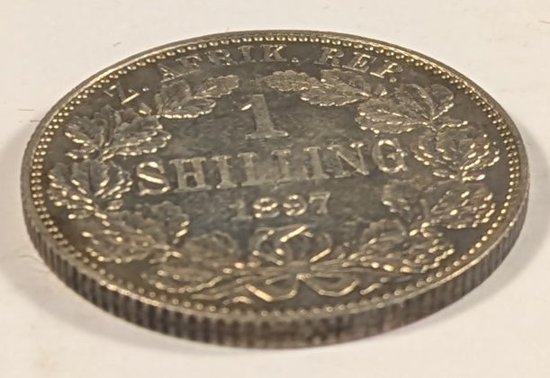 SOUTH AFRICA, Zuid Afrikaansche Republik ~ 1897 ~ Shilling ~ Bust of Paul Kruger left ~ Value divides date in wreath, Z. AFRIK. REP. above.  ~ Y-4, KM-5 ~ Nice unc., a few marks